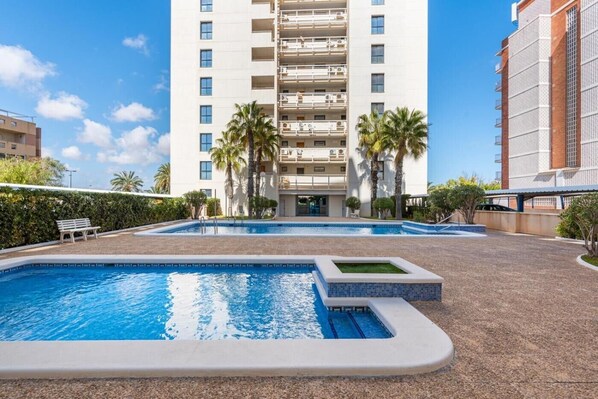 Un hôtel doté d’une piscine, de palmiers et d’un immeuble à plusieurs étages avec des balcons.