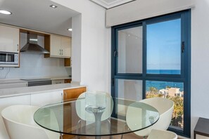 A modern kitchen with white cabinets, a microwave, and a glass dining table with chairs.