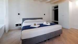 A modern bedroom with a large bed, built-in wardrobe, and a bench by the window. - Apartment 'Flat 4' with Lake View, Wi-Fi and Air Conditioning (Salò)