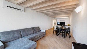 A modern living room with a grey sofa, wooden flooring, a dining area with a table and chairs, and a kitchen in the background. - Apartment 'Flat 4' with Lake View, Wi-Fi and Air Conditioning (Salò)