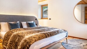 Ein Schlafzimmer mit einem großen Bett, einer Holzbalkendecke, einem kleinen Fenster und einem runden Spiegel an der Wand.
