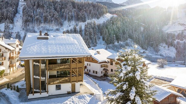 Ein schneebedecktes Bergresort mit einem Chalet-ähnlichen Gebäude, einer Seilbahn und einem markanten Berggipfel im Hintergrund.