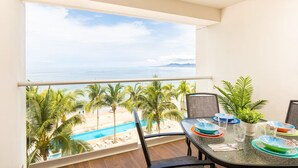 A balcony with a view of a beach and pool, furnished with a table set for dining. - Serene Beachfront Escape – Includes Delicious Breakfast (Puerto Vallarta)
