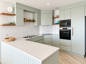 A modern kitchen with light green cabinetry, a central island, a built-in oven, and a microwave.