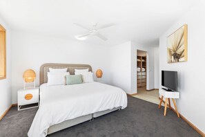 Une chambre à coucher moderne, équipée d’un lit, de tables de chevet, d’un ventilateur de plafond, d’une armoire et d’un téléviseur.
