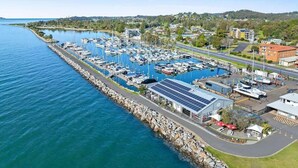 Un puerto deportivo con barcos amarrados, un edificio con paneles solares y una carretera aledaña.