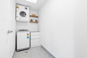 Une buanderie équipée d’un lave-linge, d’un sèche-linge et d’une petite étagère de rangement.