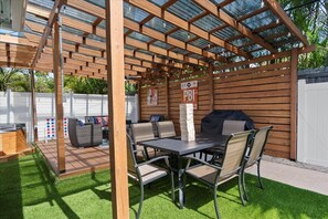 Un patio couvert comprenant une table et des chaises, un barbecue et une structure en forme de pergola en bois.