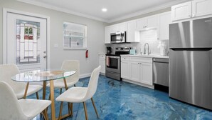A modern kitchen with white cabinets, stainless steel appliances, and a glass dining table with chairs. - Modern 2BR-Hot Tub/Pergola/Games (West Palm Beach)