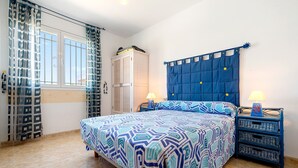 A bedroom with a bed, two bedside tables, a wardrobe, and a window with curtains.
