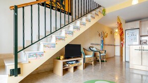 A staircase with a TV stand at the bottom, a dining area with chairs, and a kitchen area with cabinets.