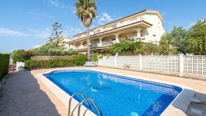A swimming pool with a white fence, a palm tree, and a multi-story building with balconies.