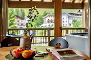 A wooden table with a bowl of fruit, a vase with a plant, and a book with a heart-shaped design.