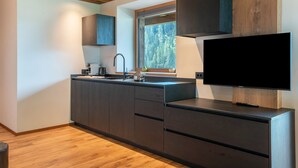 A modern kitchen with dark cabinetry, a built-in stove, and a large window overlooking a forest. - Villa Sofia Apartment 'I' with Mountain View, Private Terrace and Wi-Fi (Selva di Val Gardena)