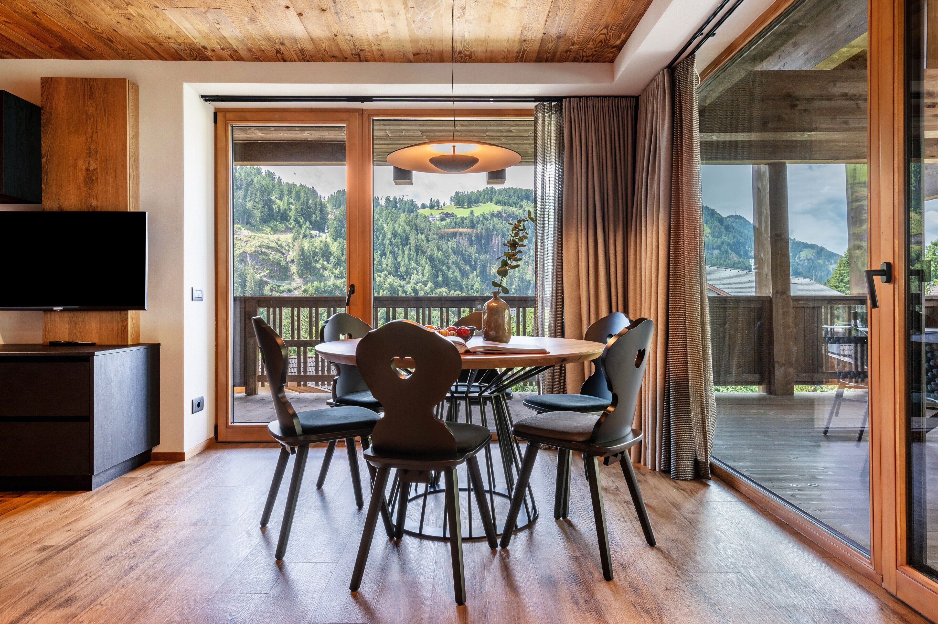 Un espace repas comprenant une table, des chaises et donnant sur une colline boisée.