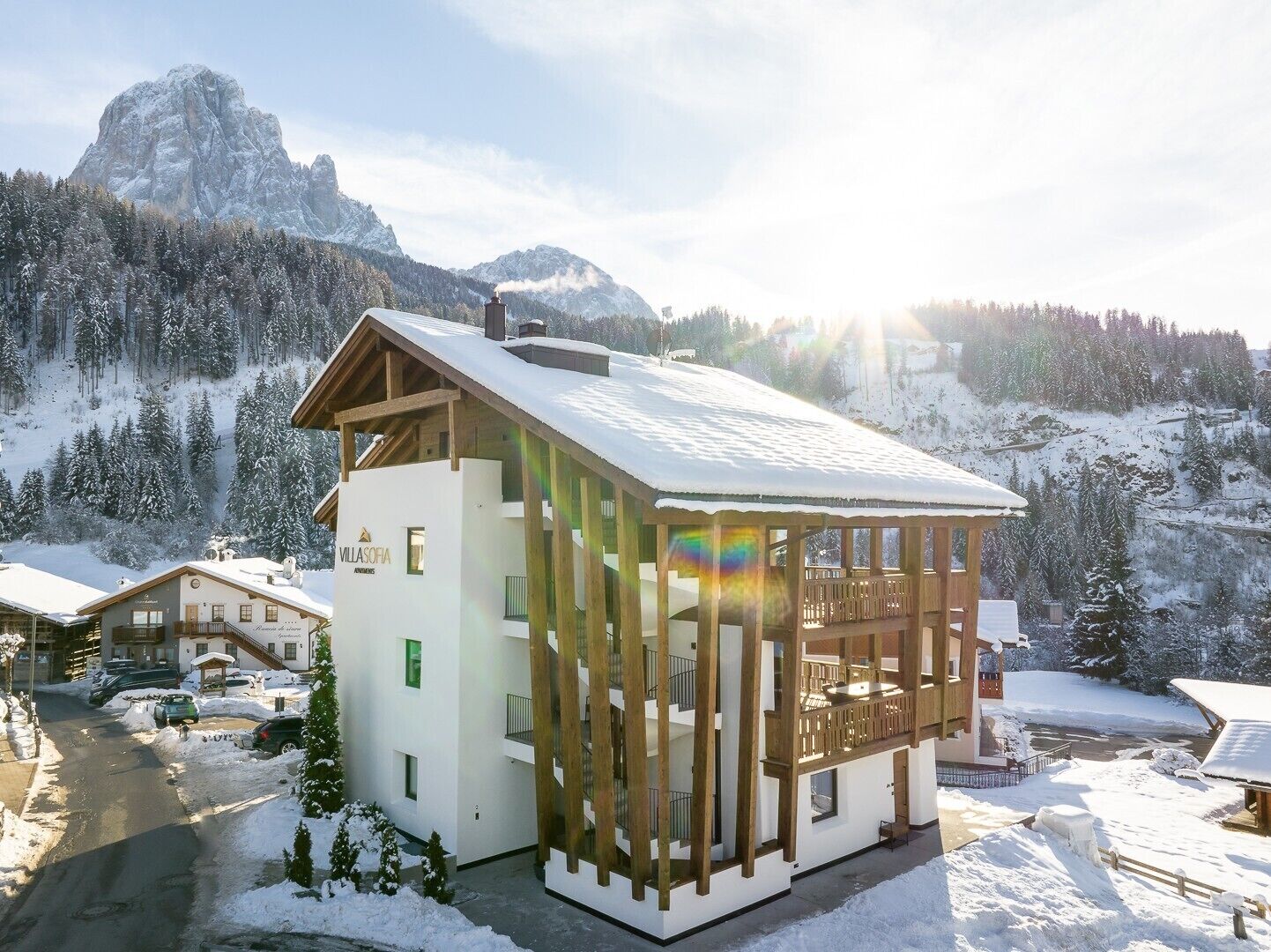 Eine moderne Villa mit Holzbalkon, umgeben von schneebedeckten Bergen und einem klaren Himmel.