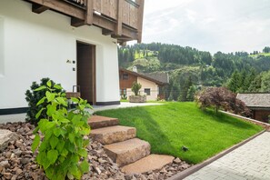 Une maison moderne avec un escalier en pierre menant à une porte en bois, entourée d’une pelouse bien entretenue et offrant une vue sur un paysage vallonné.