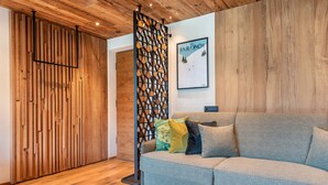 A modern living room with a wooden floor, a grey sofa with cushions, a patterned wall divider, and a poster on the wall. - Villa Sofia Apartment 'I' with Mountain View, Private Terrace and Wi-Fi (Selva di Val Gardena)