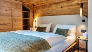 Un plafond en bois, un lit avec une literie blanche, une table de chevet avec une lampe et une étagère.