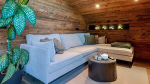 Une pièce avec un canapé bleu clair, un plafond en bois, une grande plante verte, une table ronde en bois et un luminaire fixé au mur.