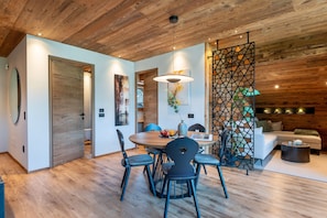 A modern interior with a wooden ceiling, a round dining table with chairs, a sofa, and a decorative partition.