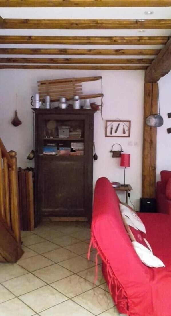 Une pièce avec un plafond en bois, un canapé rouge, une porte en bois et une étagère contenant des ustensiles de cuisine.