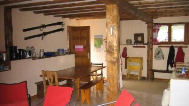 Ein Essbereich mit Holztisch und roten Stühlen, ein Küchenbereich mit Herd und Schränken sowie ein Fenster mit Blick.