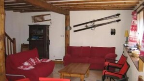 Ein gemütliches Wohnzimmer mit Holzboden, roten Sofas, einem Couchtisch aus Holz und Ski, die an der Wand hängen.