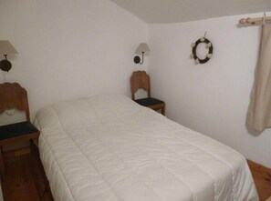 A bedroom with a bed, two nightstands, a wall-mounted lamp, a small table, and a wall decoration. - Chalet 'Les 3 Vallées' with Wi-Fi (Les Belleville)