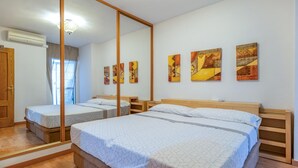 Habitación de hotel con dos camas, cabeceros de madera, un espejo grande y tres cuadros abstractos en la pared.