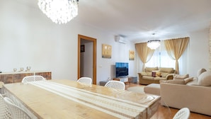 Una sala moderna con comedor, sofá, televisor y candelabro.