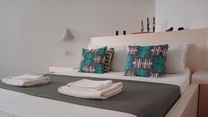 Una cama bien hecha con sábanas blancas y dos almohadas estampadas, una mesita de noche y una lámpara de pared.