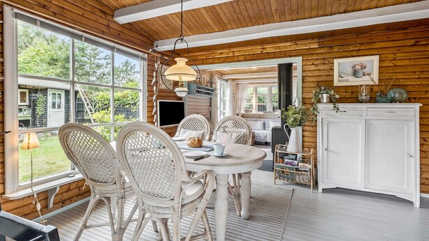 A cozy wooden interior with a dining area featuring wicker chairs, a round table, and a white cabinet.