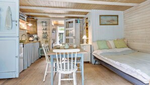 A cozy, compact room with a wooden ceiling, a dining table with chairs, a bed, and a kitchen area with cabinets and a sink.