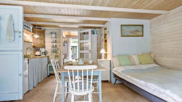 Una camera accogliente e compatta con soffitto in legno, un tavolo da pranzo con sedie, un letto e un angolo cottura con pensili e lavello.