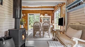 Een gezellig chaletinterieur met een houtkachel, rieten stoelen, een bank en een televisie.