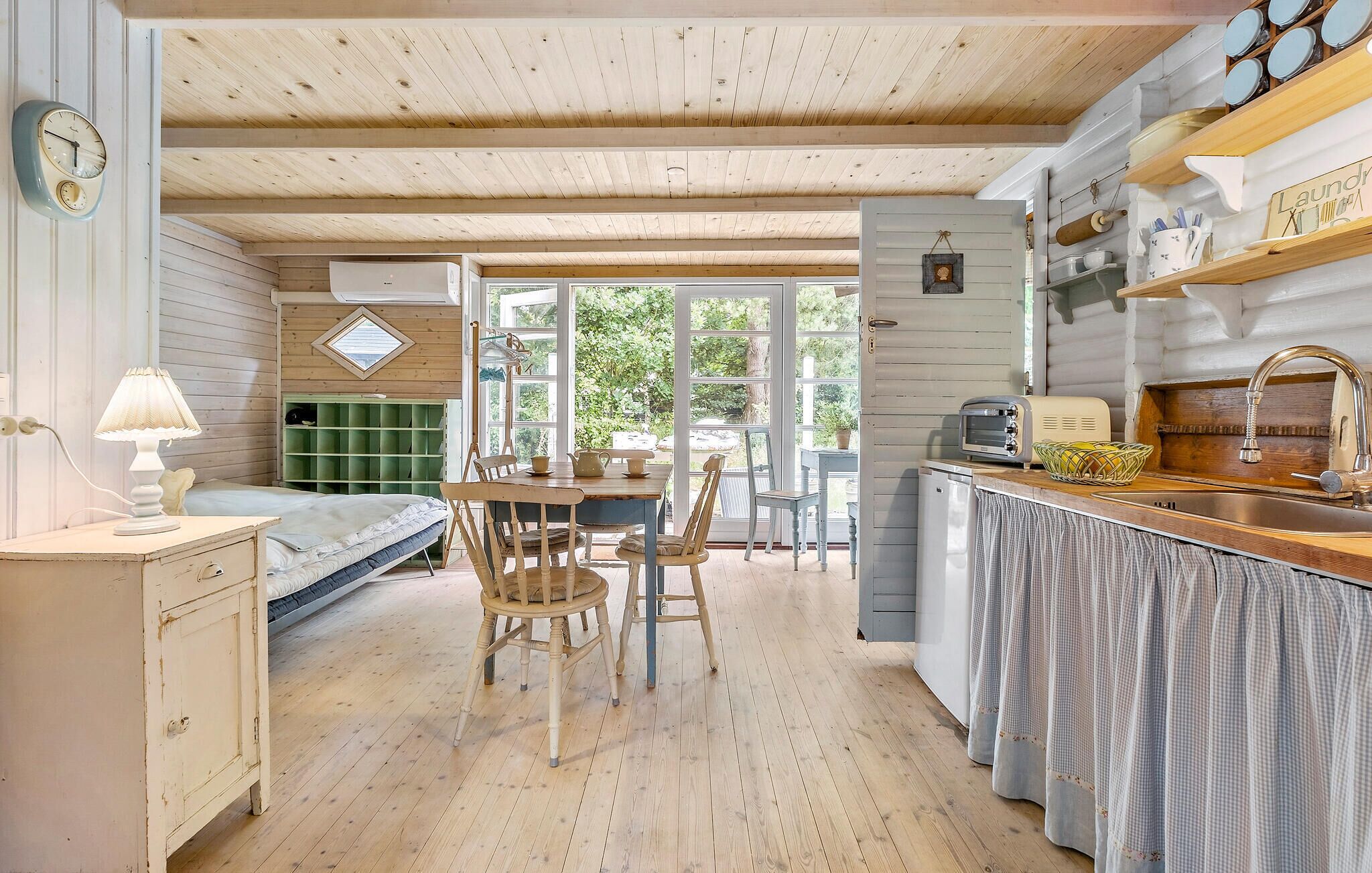 Une chambre confortable, aménagée dans le style d’un chalet, avec un plafond en bois, une table à manger avec des chaises, un petit coin cuisine et un lit doté d’une tête de lit verte.