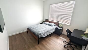 A bedroom with a bed, a desk, and a window with blinds.