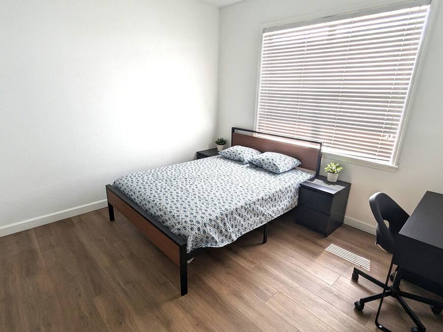 A bedroom with a bed, a desk, and a window with blinds.