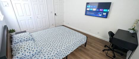 A bedroom with a bed, a desk, and a TV mounted on the wall displaying streaming services.
