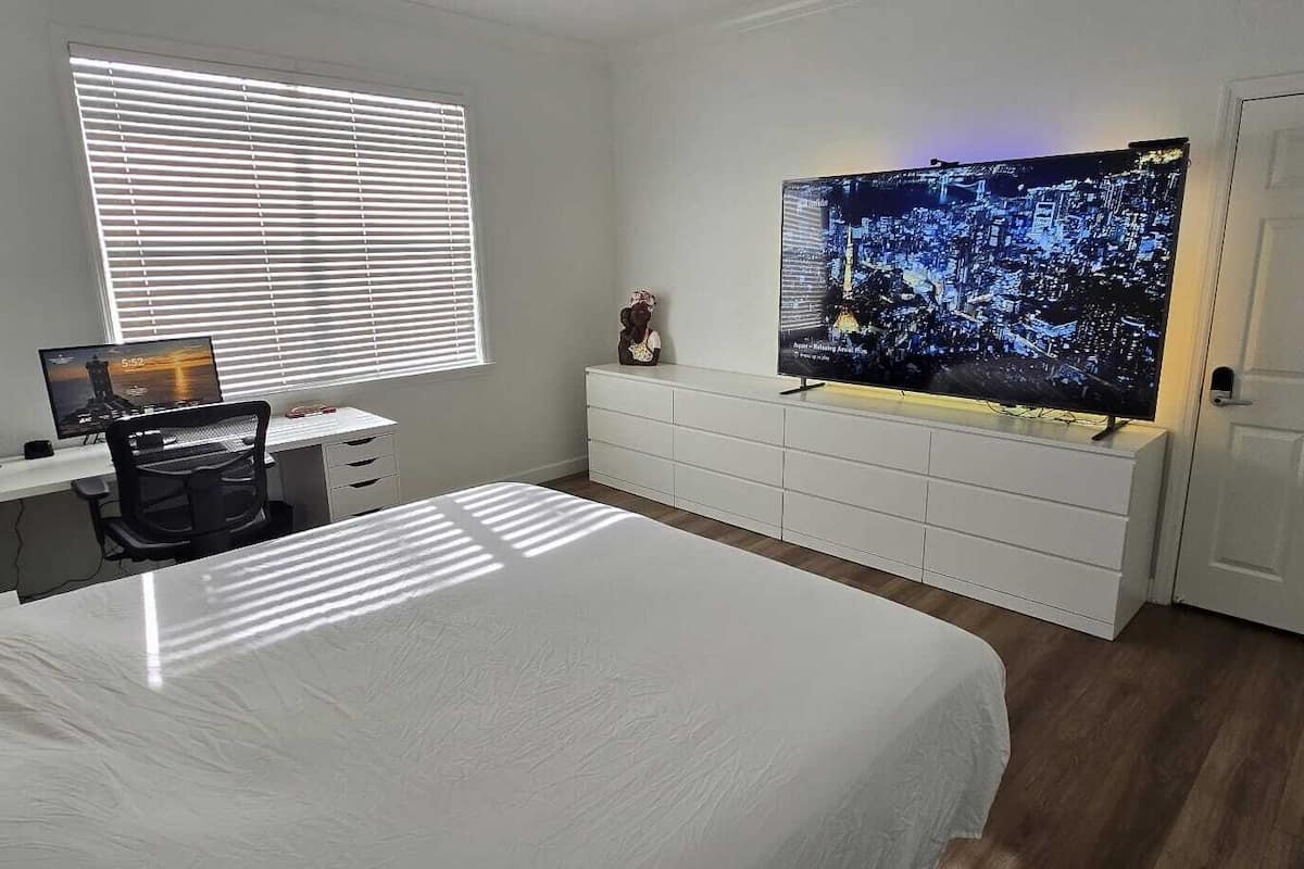Un dormitorio con cama, un escritorio con computadora, un televisor y un aparador.