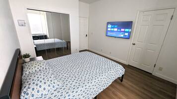 A bedroom with a bed, a TV mounted on the wall, a door, and a window with blinds.