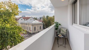 A balcony with a view of a historic building, a potted plant, and a table with a chair.