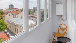 A narrow balcony with large windows, a white wall, a radiator, a wooden chair, and a small table.