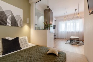 Ein modernes Schlafzimmer mit Bett, einem großen Spiegel, einer Hängeleuchte und Blick auf eine Stadtlandschaft durch transparente Vorhänge.