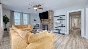 Una sala de estar con un sofá, una chimenea, un televisor y un ventilador de techo.