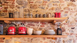 Una cocina rústica con pared de piedra, estantes de madera, un robot de cocina rojo antiguo y un grifo de bronce.