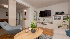 A living room with a grey armchair, a round coffee table with a plant, a bookshelf, and a flat-screen TV. - Amazing home in Prolozac Donji (Prolozac Donji)