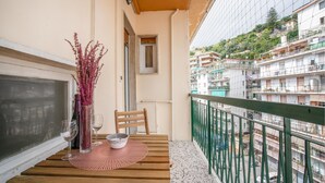 Un balcón con una mesa de madera, dos sillas, un florero con flores y vistas a una zona residencial con edificios de varios pisos.