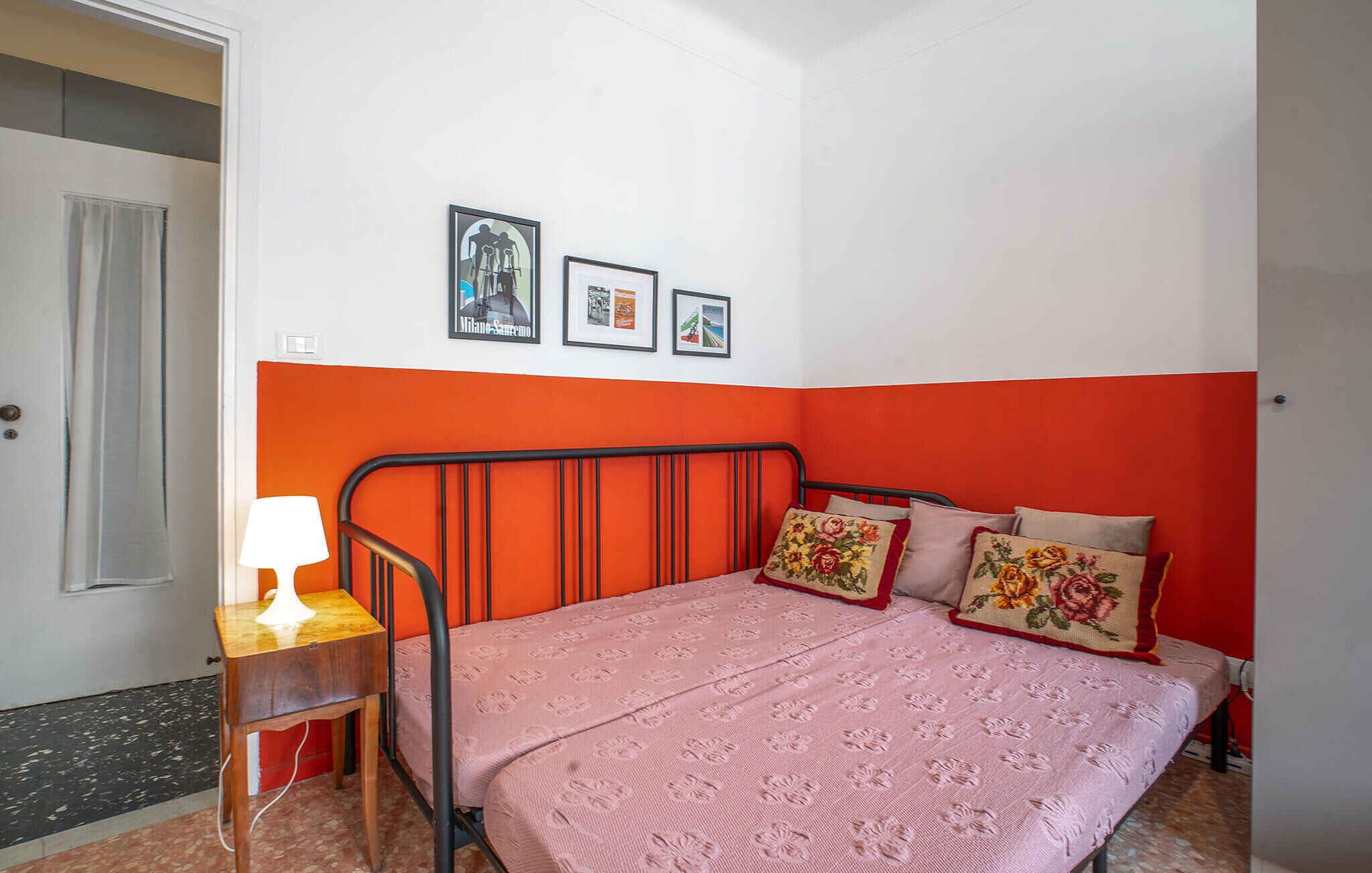 A bedroom with a bed, a nightstand, and a lamp. There are three framed pictures on the wall.